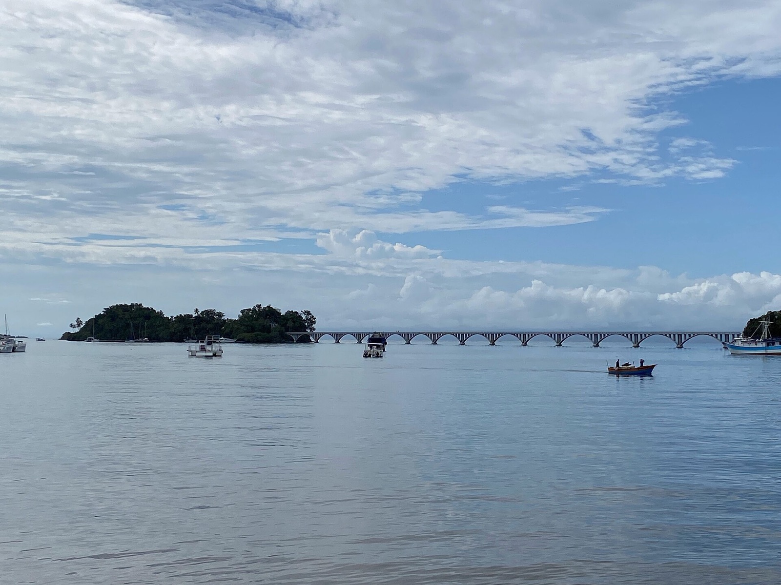 The calm water of Samaná Bay with small islets and the footbridge to Cayo Vigía under a cloudy sky